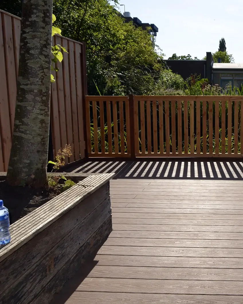 Ná: composiet vlonder met plantenbak en een houten hekwerk langs het water